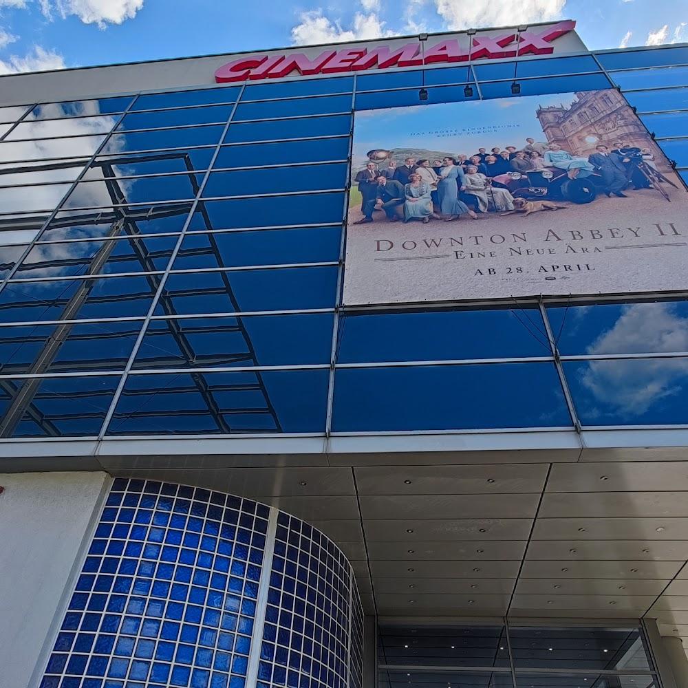 A modern glass building with a Cinemaxx sign and a poster for Downton Abbey II.